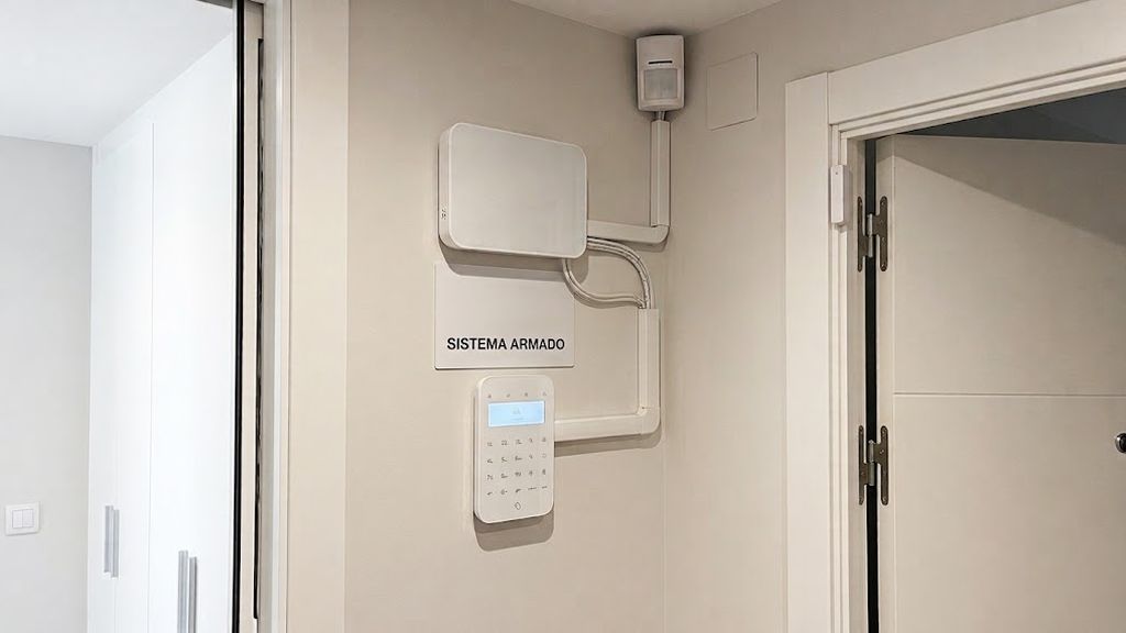 Central de alarma con teclado y detector de movimiento instalados junto a la puerta de entrada de un local